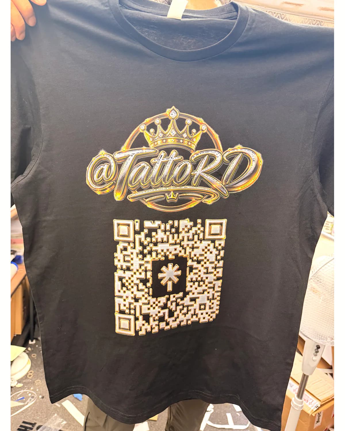 Black polo held in the workshop with gold branding and a large QR code